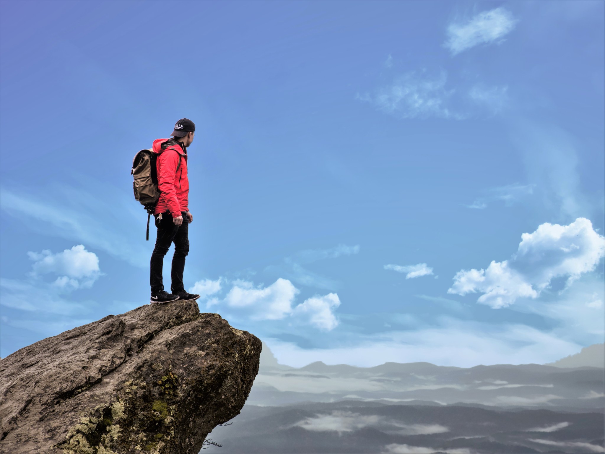 Male hiker standing on the precipice of a chasm contemplating his future.
