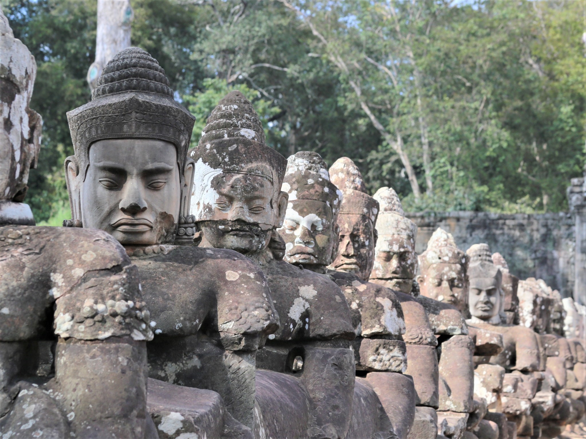 A row of stone statues with sombre facial expressions at Angkor, Cambodia.
