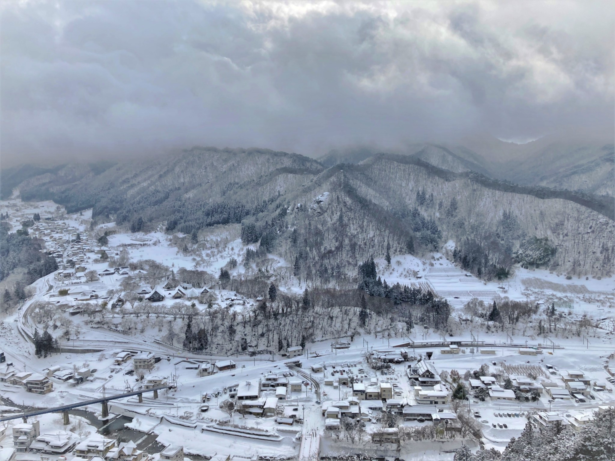A winter view of the Japanese town of Yamadera covered in snow, situated in front of barren mountains on a cloudy day.