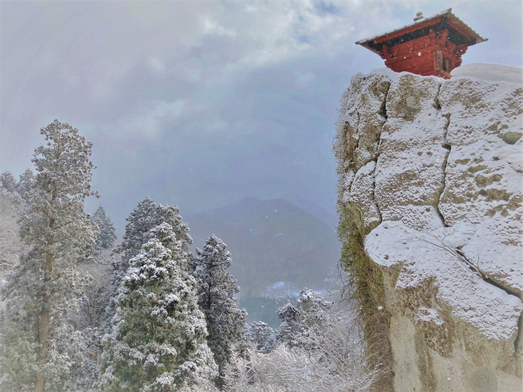 A winter view of a red wooden sutra repository perched on the edge of a cracked and icy cliff at Risshaku-ji in Yamadera, Japan.