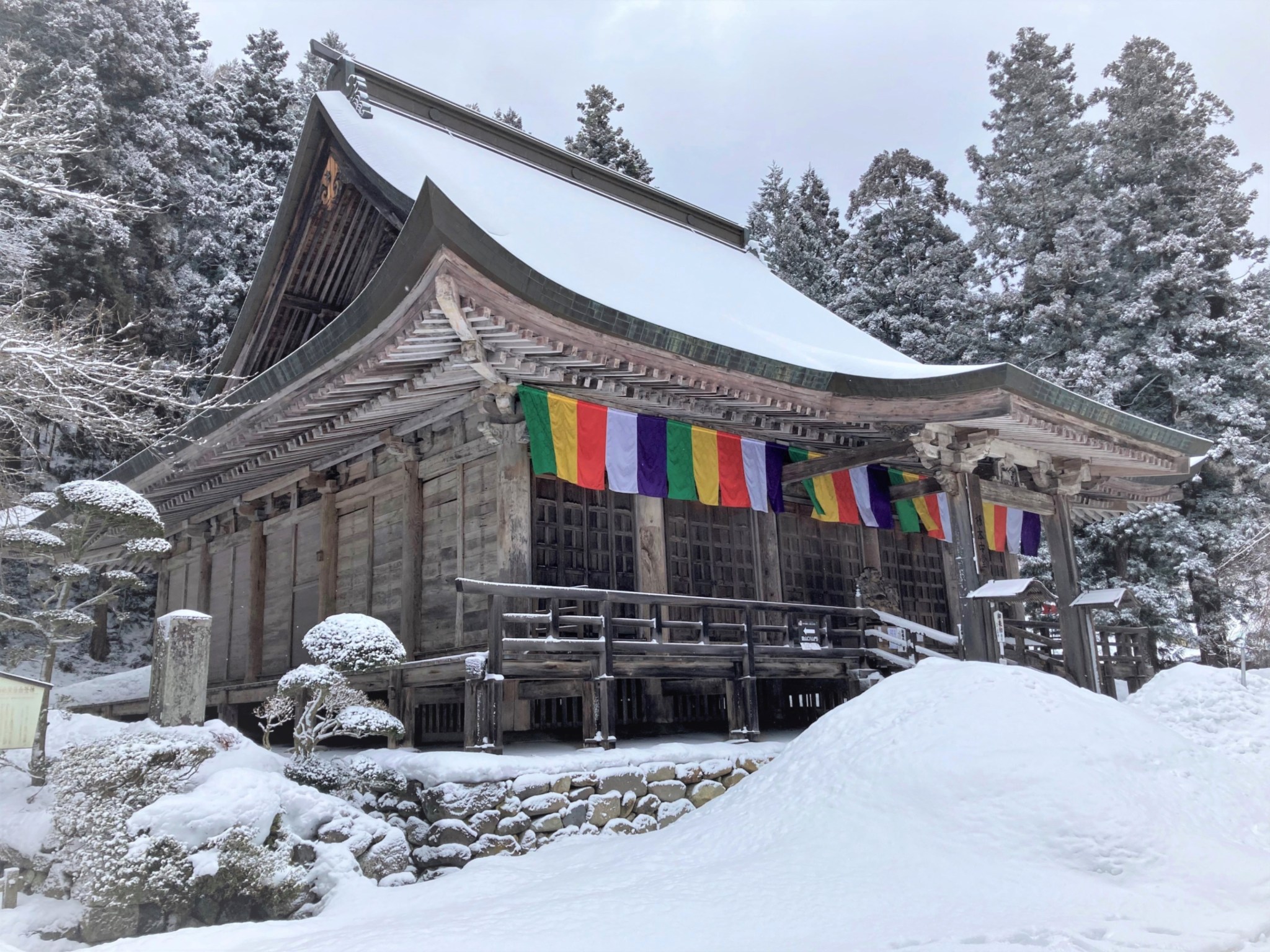 A large ornate Japanese Buddhist temple situated in front of a snowy forest.
