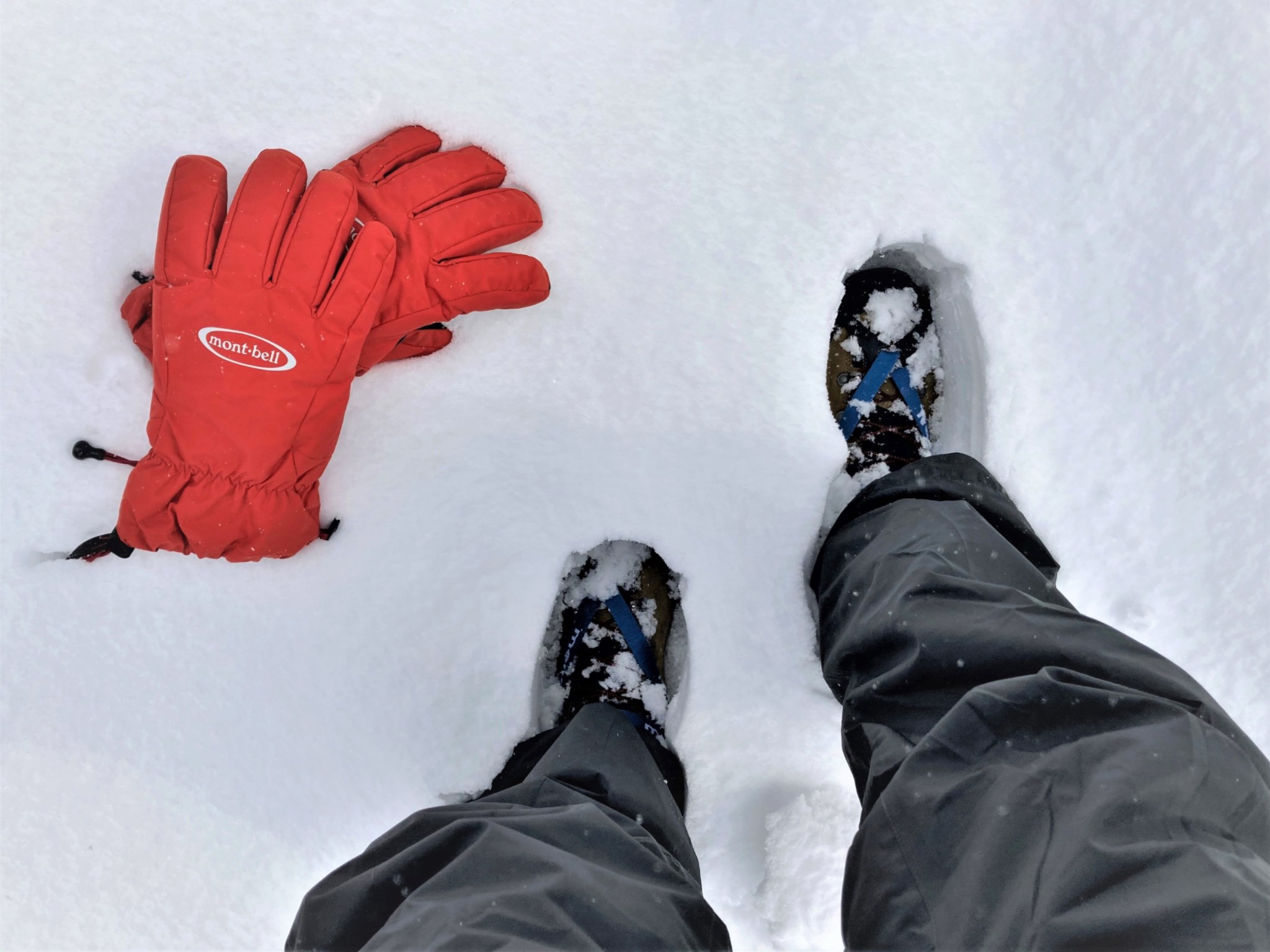 A man walking through deep snow with crampons and bright red gloves.