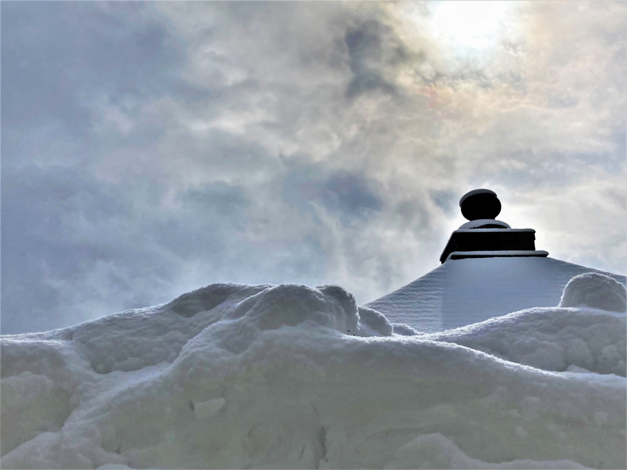 The winter sun piercing the clouds over the roof of a Japanese Buddhist temple and a large bank of snow.