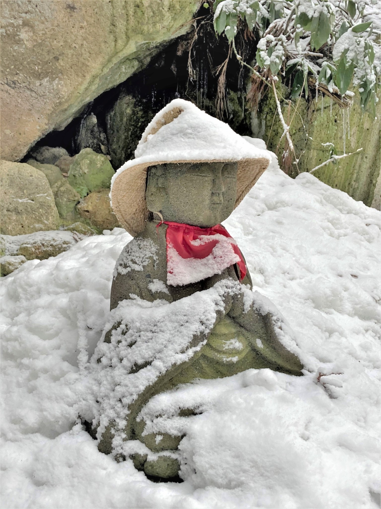 A seated stone Buddhist Jizo statue partially covered in snow at the Japanese temple complex of Risshaku-ji.