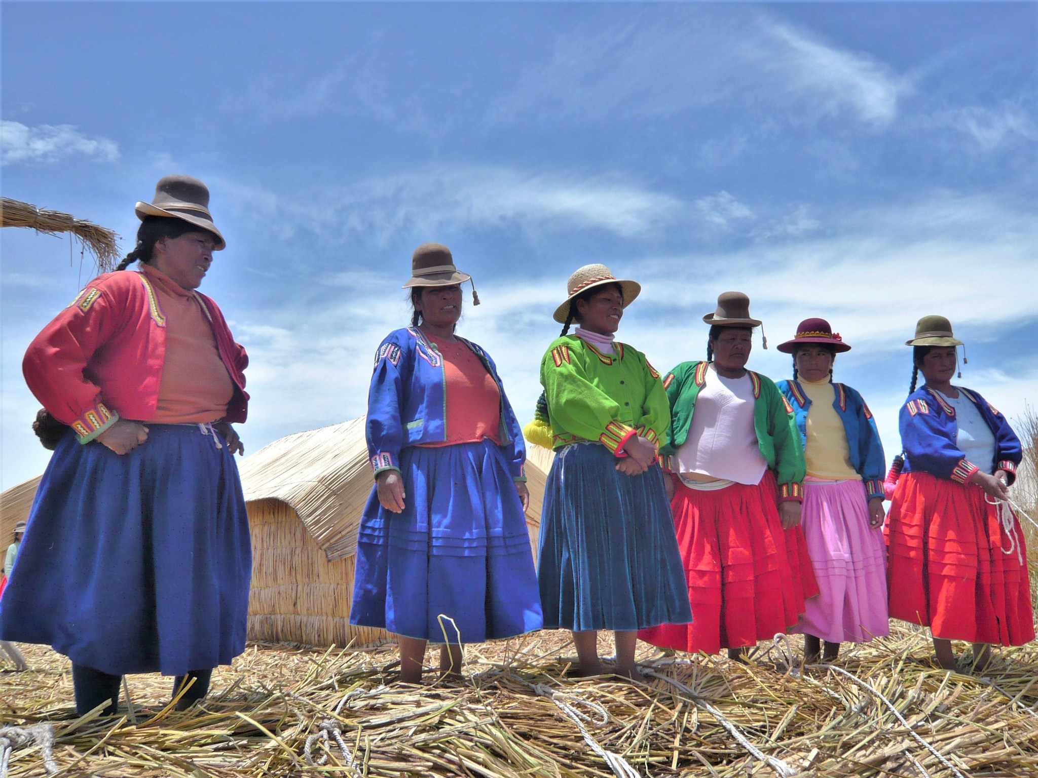 A group of Peruvian women in colourful traditional dress standing on an island of reeds.