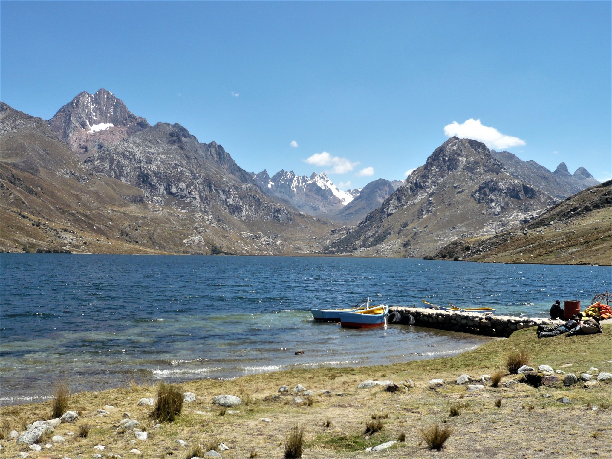 A scenic view of a two boats on lake surrounded by partially snow-capped mountains.