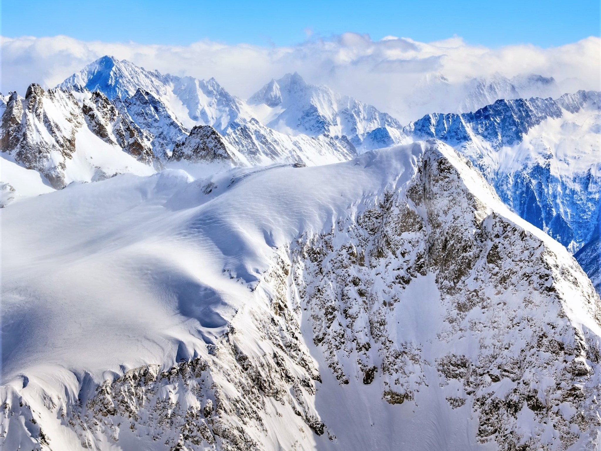 A collection of jagged snow-covered mountain peaks beneath a blue sky.