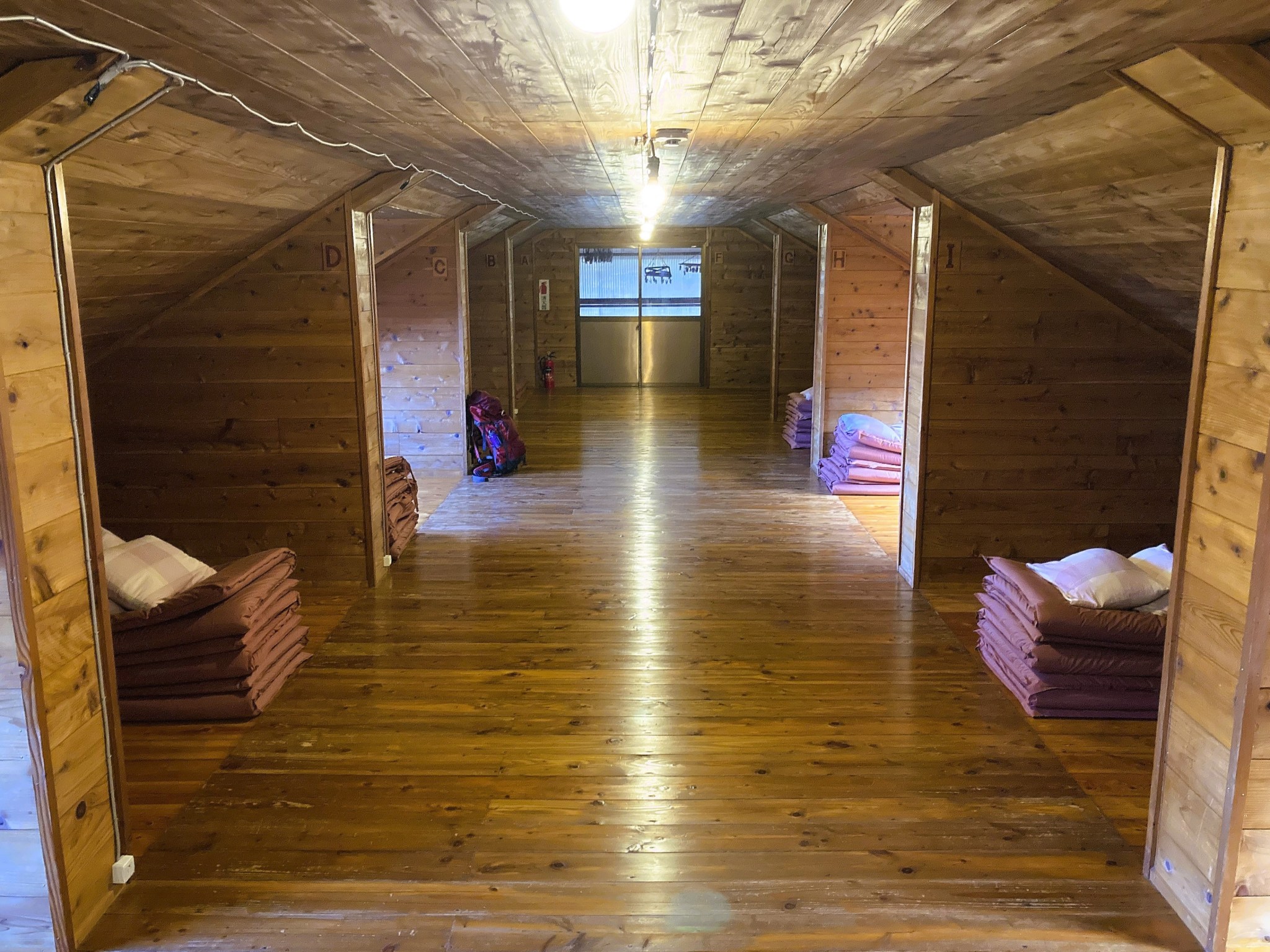 The symmetrical wooden interior of a Japanese mountain lodge containing folded and stacked futons.