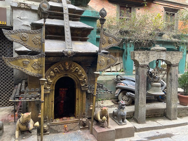 Timeworn metal statues and artwork in front of an ancient monument on a paved street in Patan, Nepal.