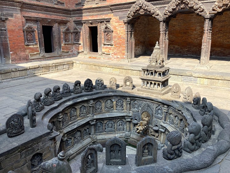An ancient intricate circular monument in the centre of a red brick-faced courtyard in Patan, Nepal.