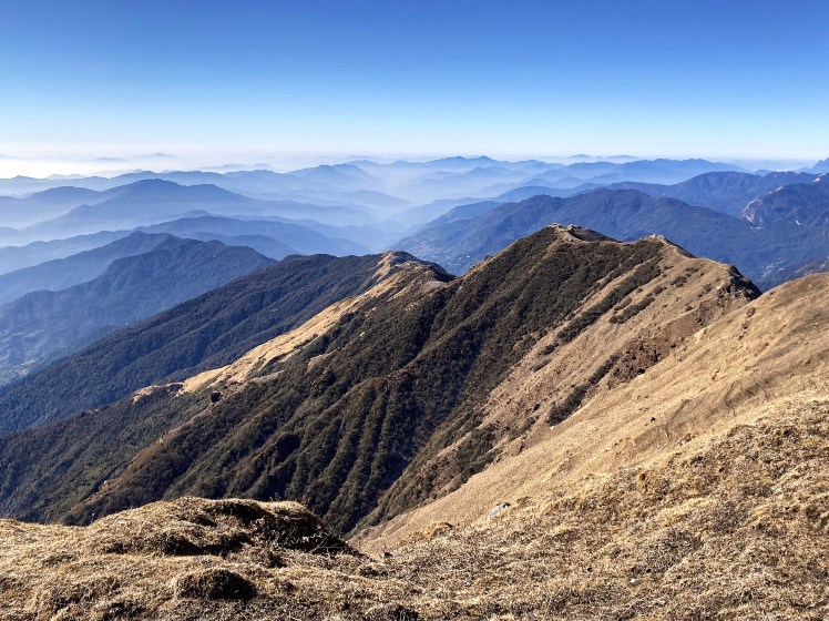 A long Himalayan ridgeline sits beneath a clear blue sky leading to a vortex of clouded valleys on the Mardi Himal trek in the Annapurna Conservation Area of Nepal.